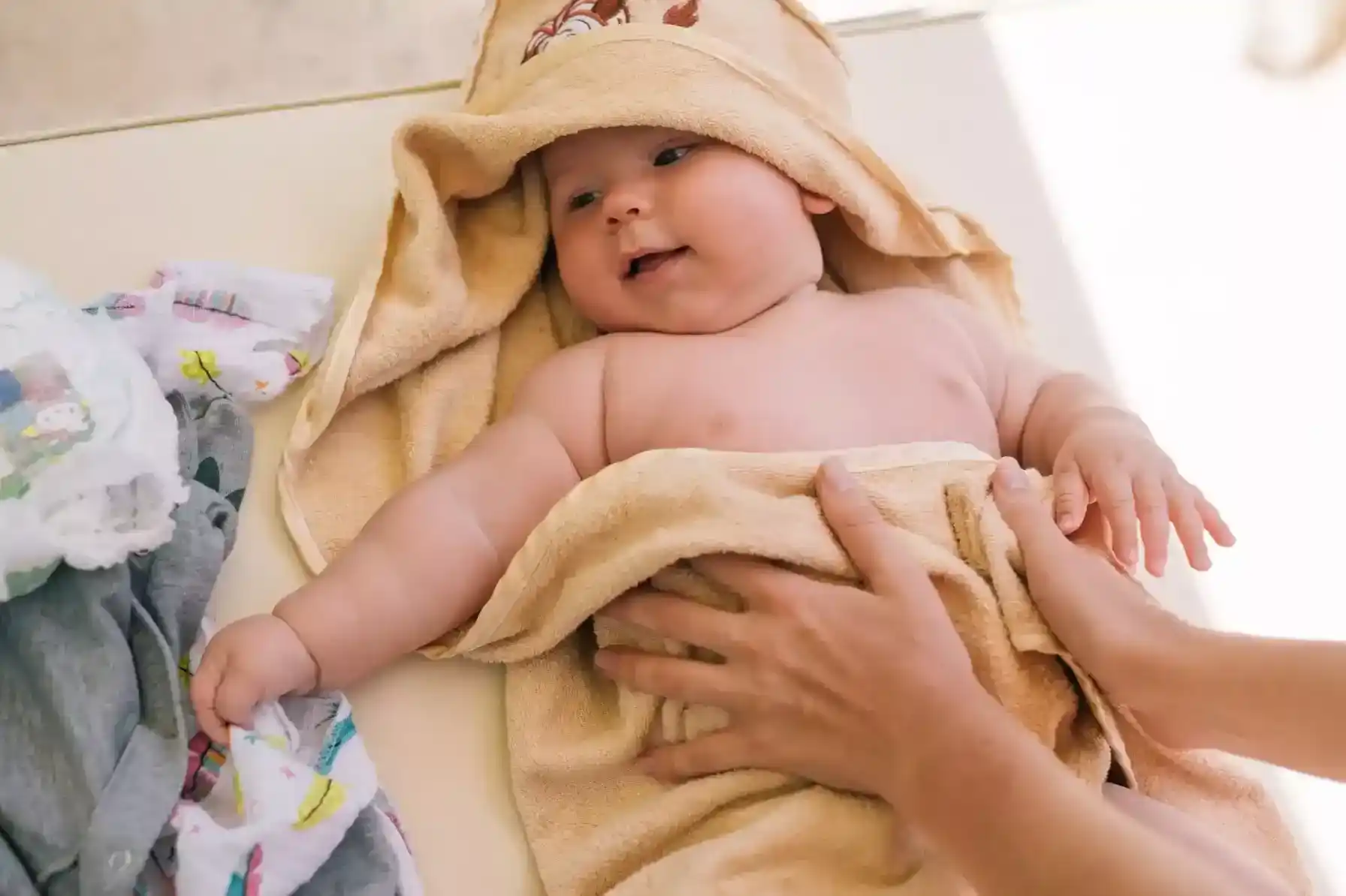 Baby smiling during a warm Baby Bath with soft sponge and towel