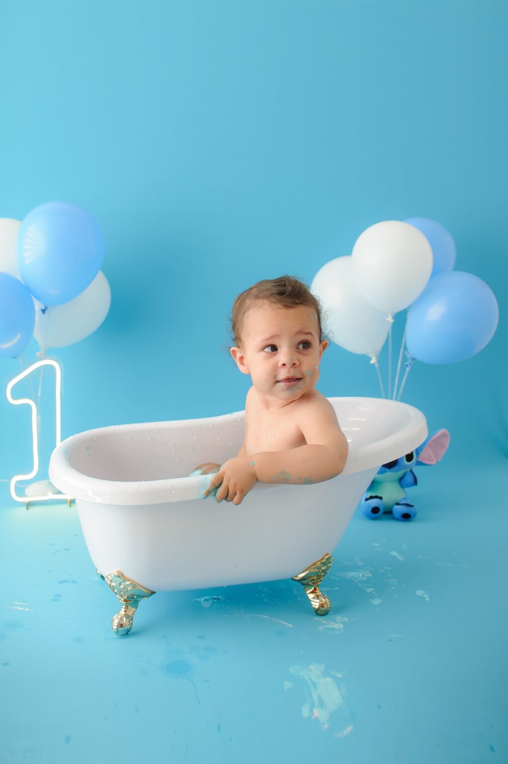 Adorable child in tub with balloons celebrating first birthday in a studio setting.
