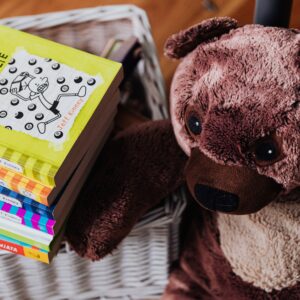 A stack of colorful children's books next to a plush teddy bear in a cozy kids' room.