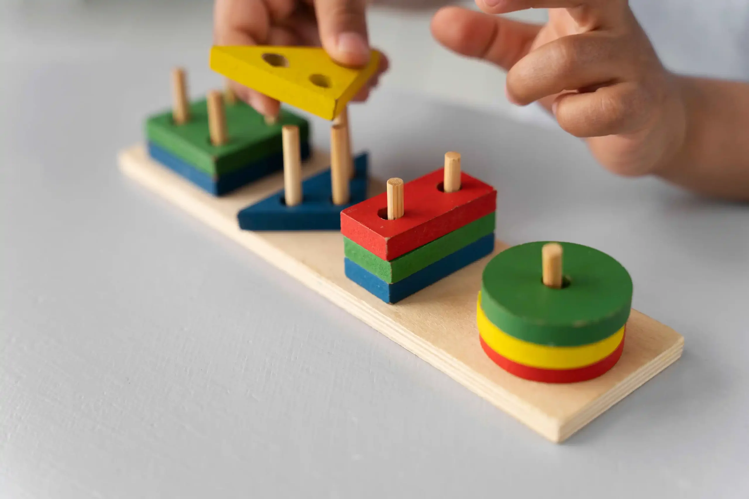 Child playing with a colorful wooden stacking toy as one of the Brain Development Toys
