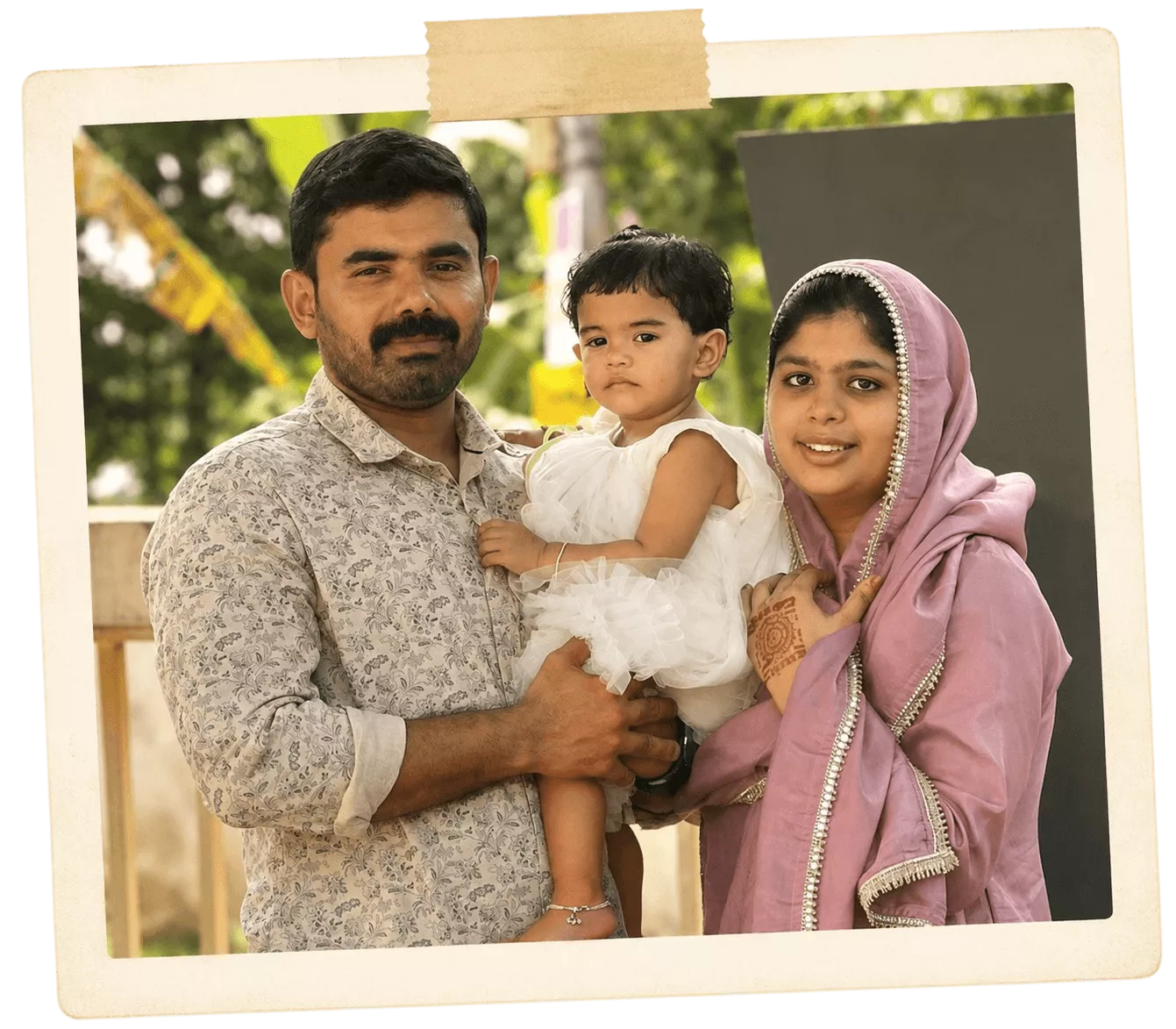 Polaroid-style outdoor family photo of a father holding his toddler daughter beside the mother