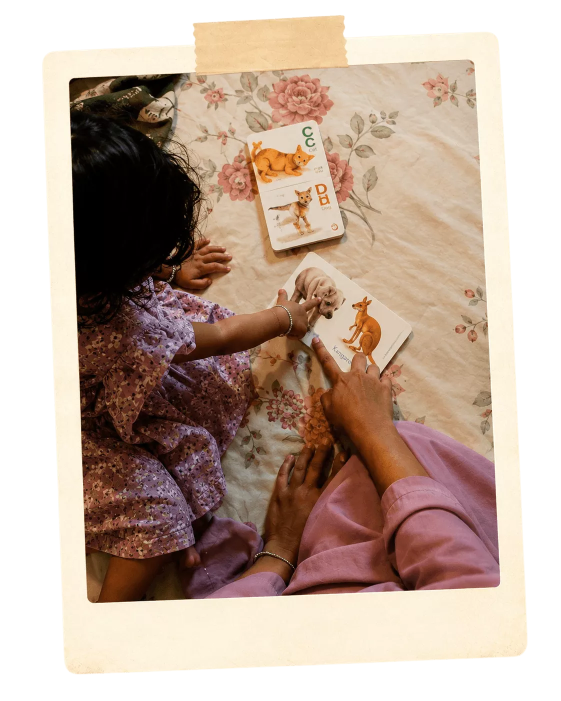 Overhead polaroid photo of a mother and daughter reading animal alphabet flashcards on a floral bedsheet