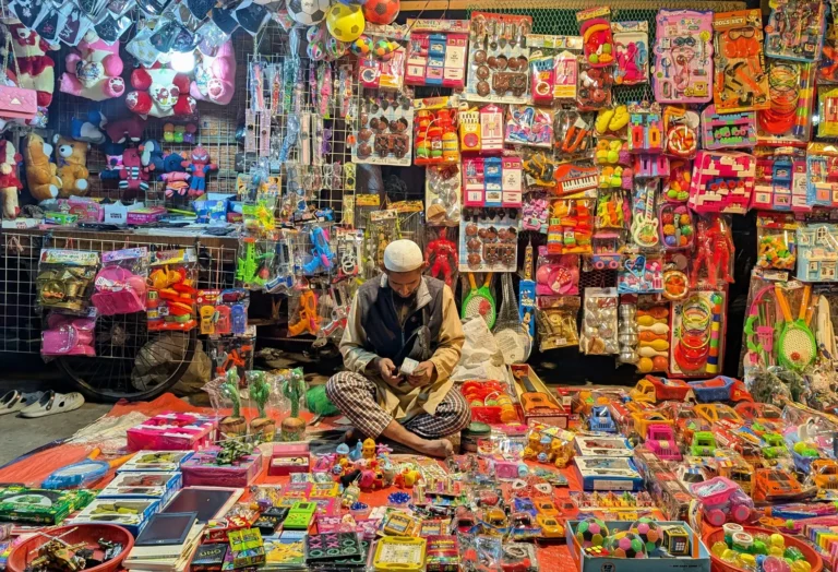 A street vendor surrounded by walls of colorful toys, illustrating the sheer volume of toys marketed to parents today