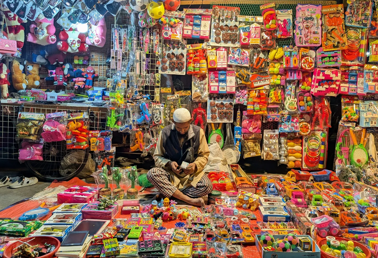 A street vendor surrounded by walls of colorful toys, illustrating the sheer volume of toys marketed to parents today